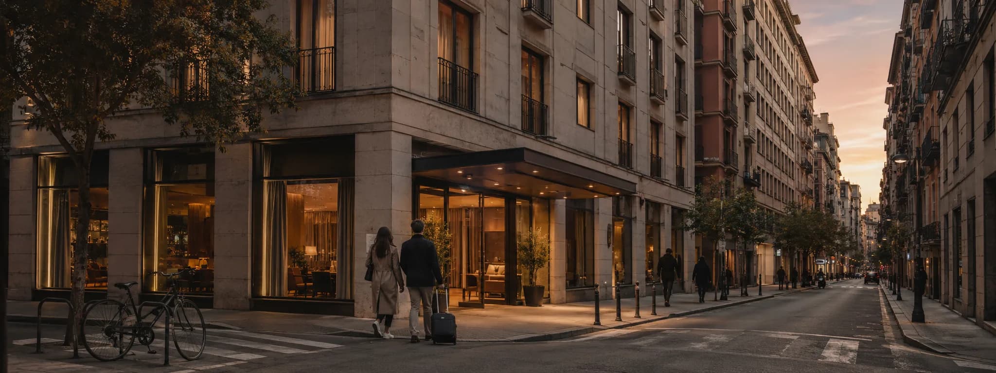 A boutique hotel on a city street corner at golden hour, guests arriving with a suitcase